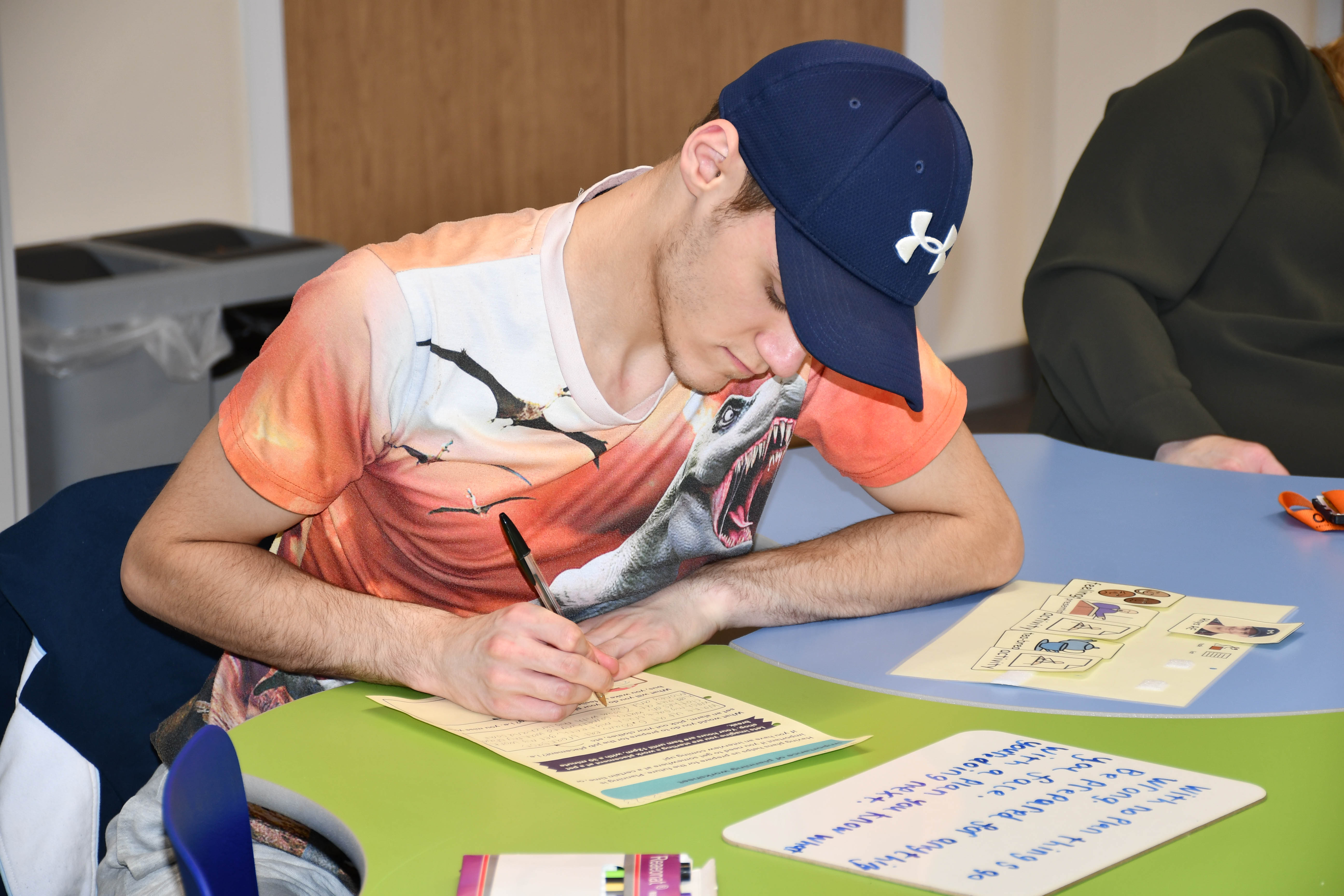 A young man fills out an application form. He is sat in a classroom.