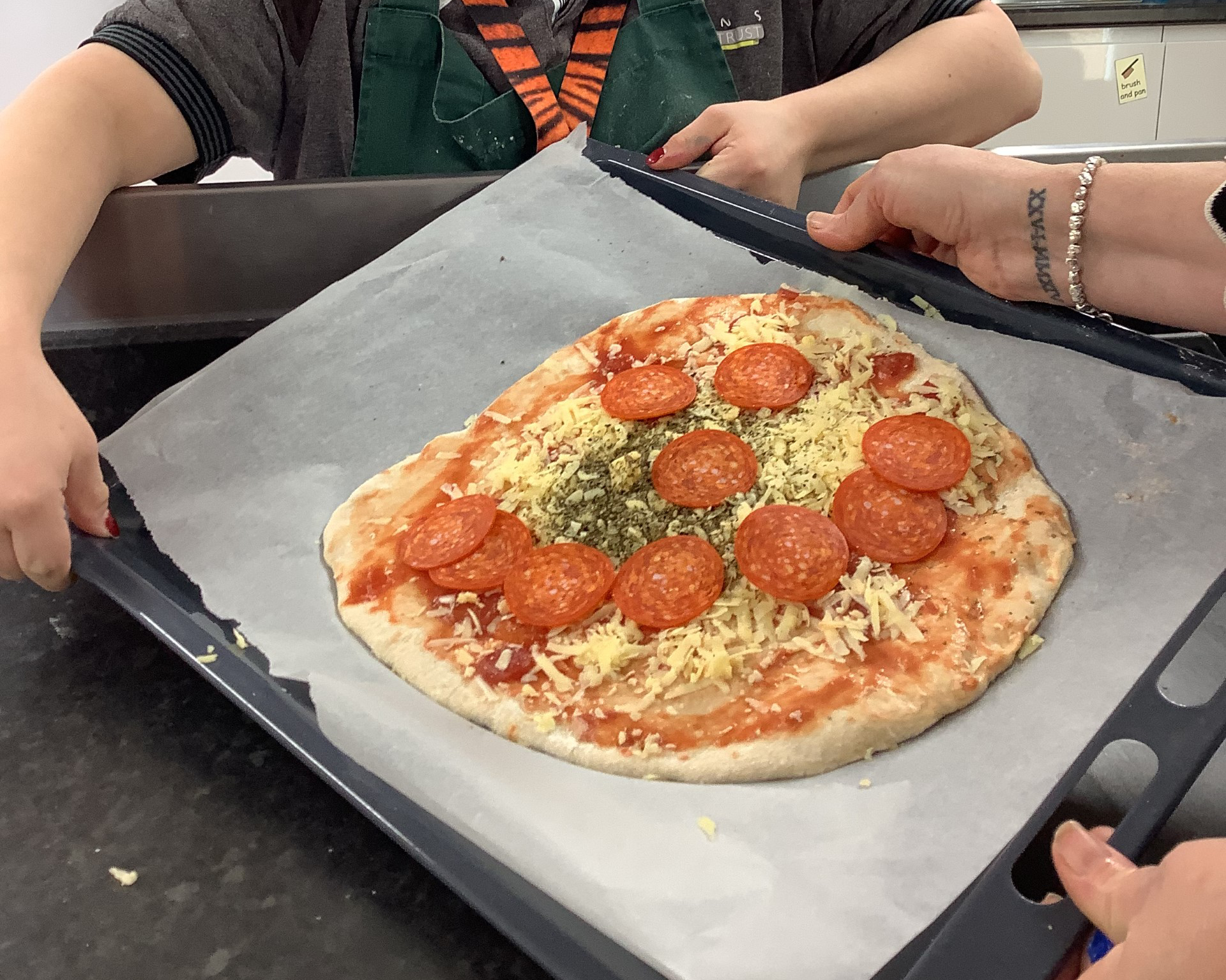 A pizza on a tray with hands.