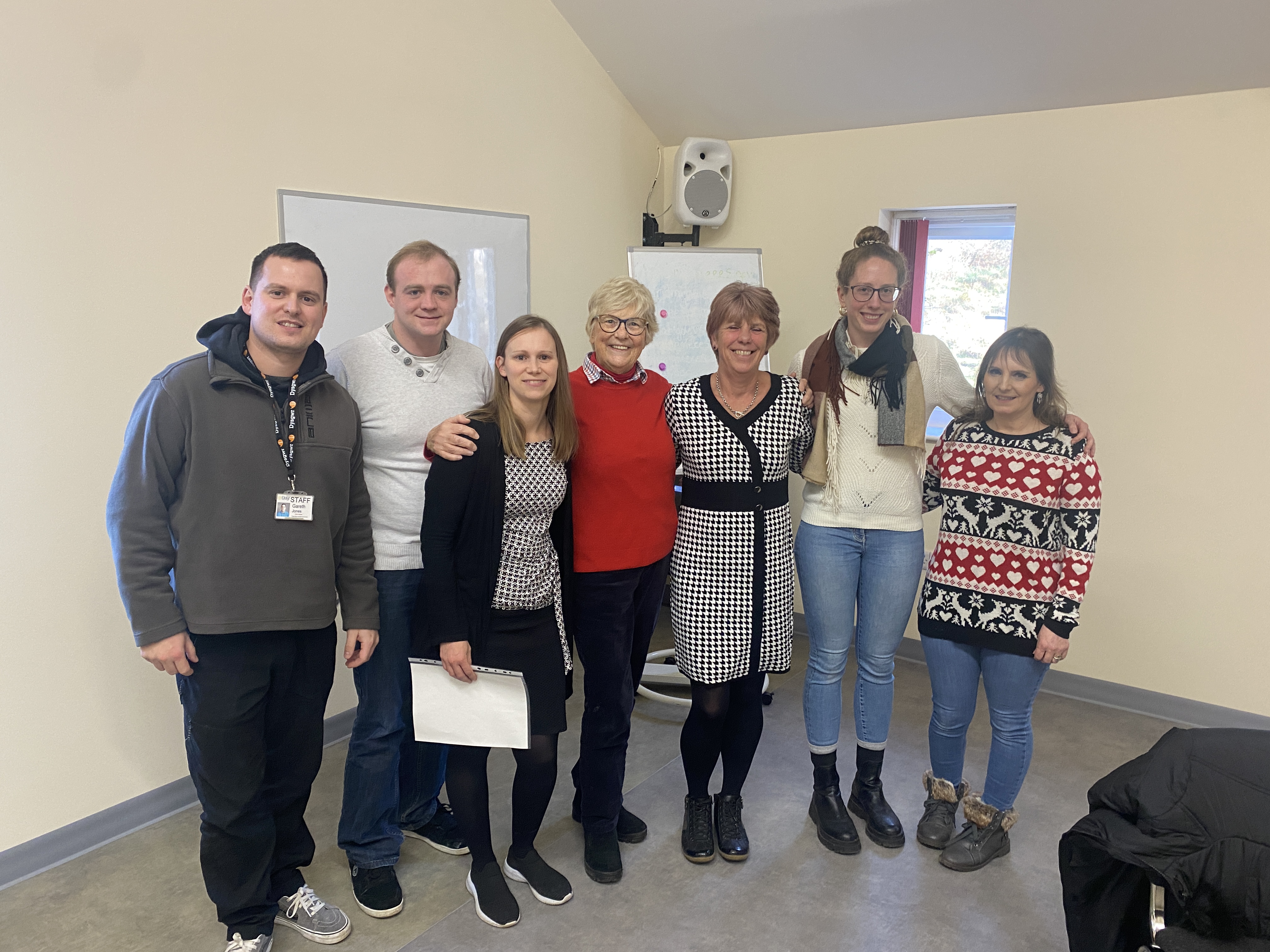 7 people in a classroom smiling at the camera. 