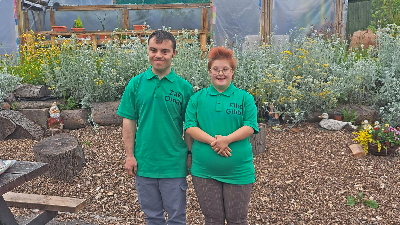 A boy and girl in green t-shirts in a greenhouse for a competition