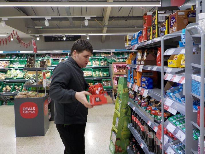 Boy stacking shelves in supermarket.