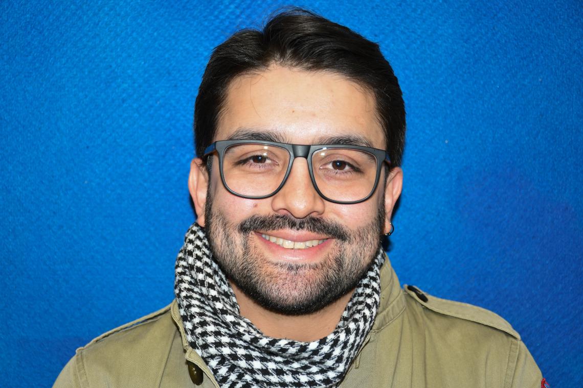 A smiling man wearing glasses in front of a blue wall.