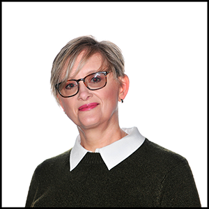 A headshot of a woman in a black jumper with a white shirt under. She is wearing black glasses