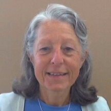 A woman in a white cardigan smiles at the camera. There is a brown background.