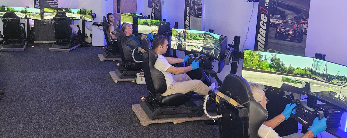 A group of people sim racing in a room. Their are computer screens.