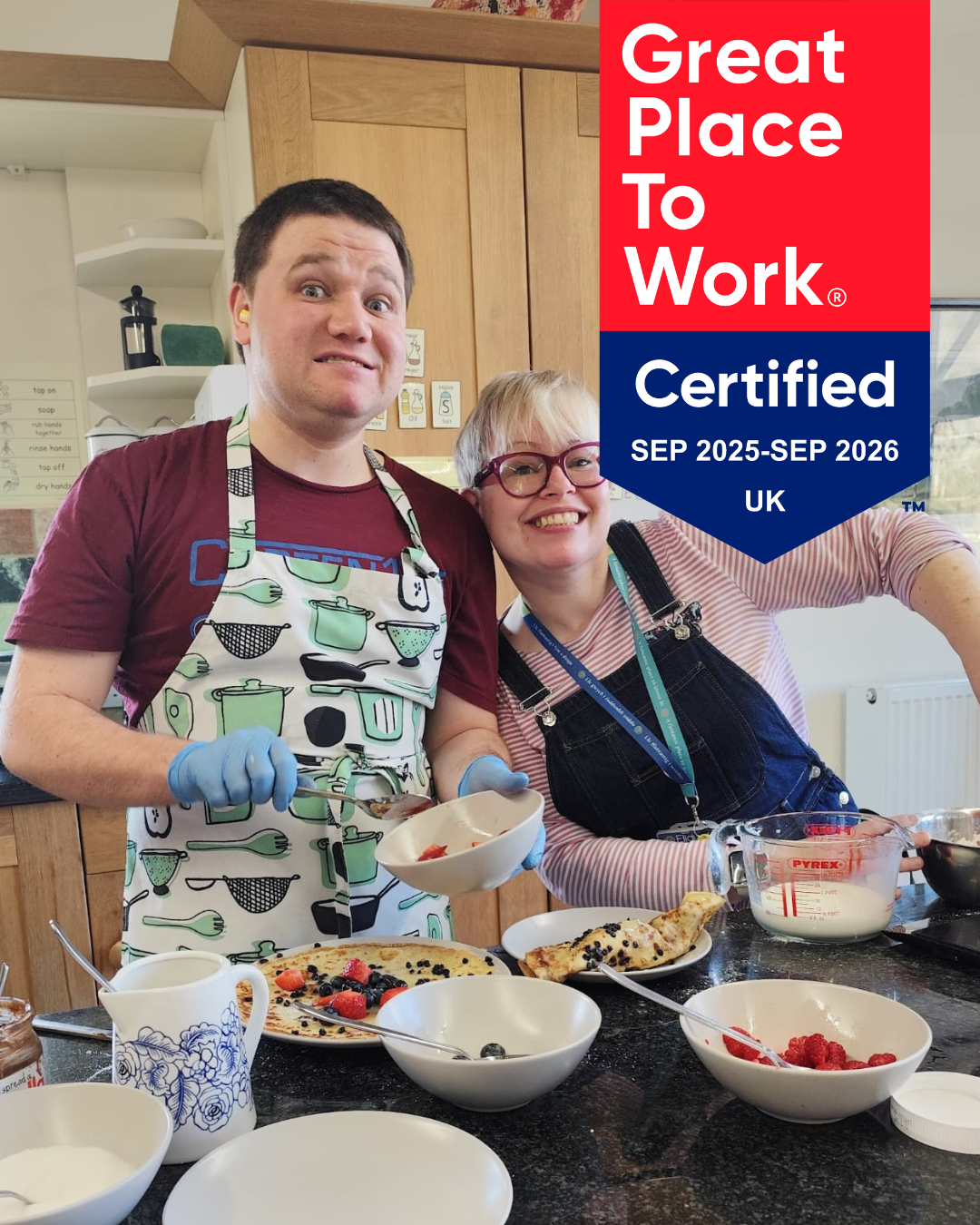 A young man and a woman wear aprons and cook in a kitchen. There is a logo - great place to work - on a red background