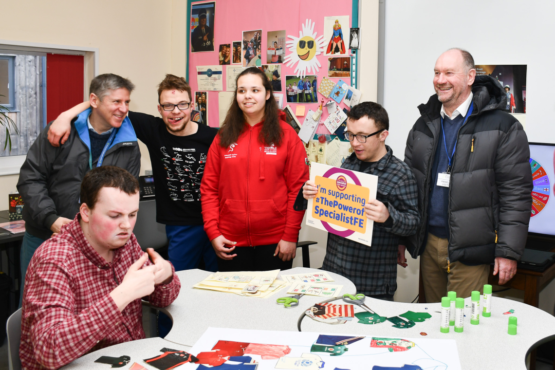 A group stood around a table smiling in a classroom.