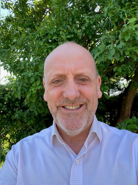 A man smiles to camera with a bush in the background