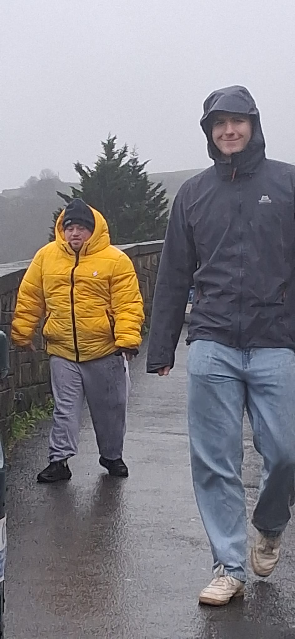 Two men walk in windy weather conditions by the beach
