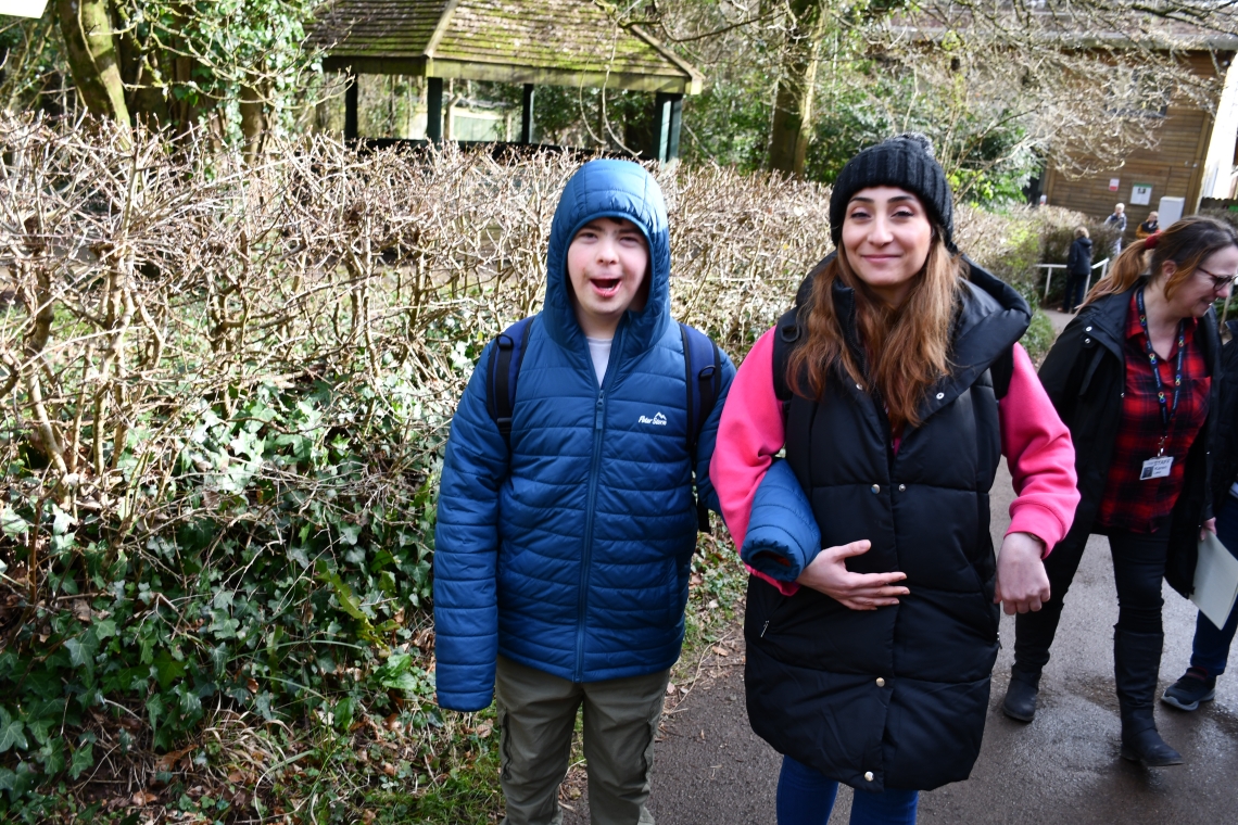 A young man is arm in arm with a member of staff. They are outside.