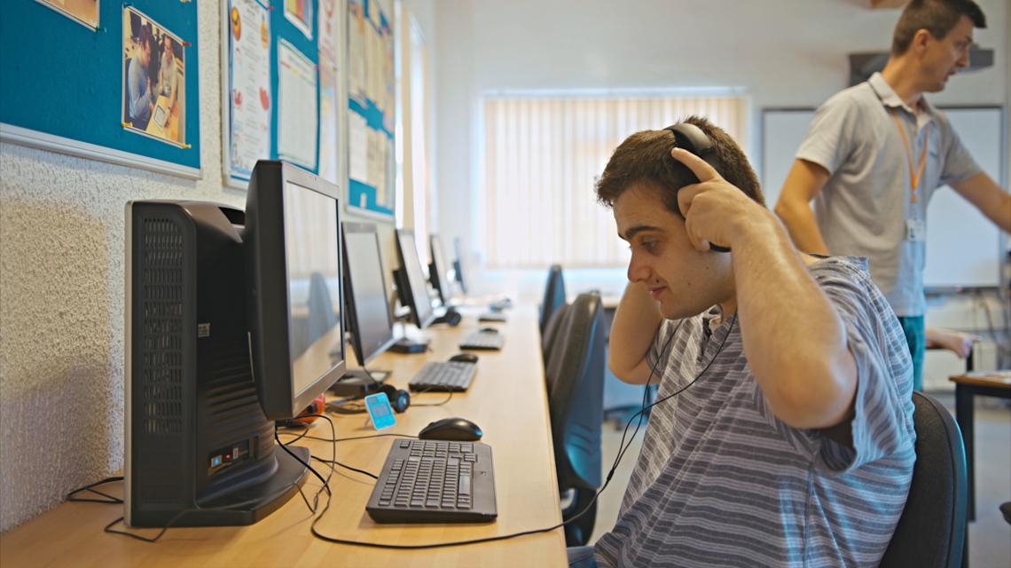 Boy on a computer putting on headphones.