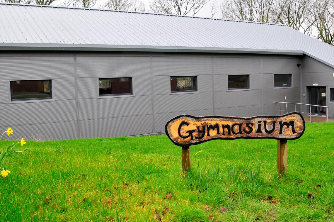 Exterior shot of gym building with a wood gymnasium sign on display