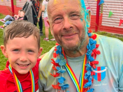 A boy and a man at a colour run. They are smiling.