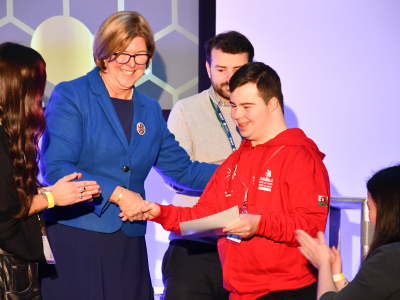 A young man shakes hands with a woman in a blue jacket on a stage