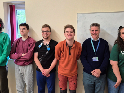 6 people stand in a row in a classroom. They are happy.