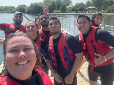 Eight people in red buoyancy aids by a lake. It is sunny