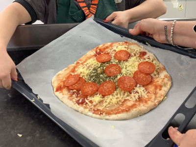 A pizza on a tray with hands.