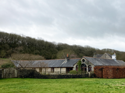 A converted barn surrounded by trees and grass. A grey sky.