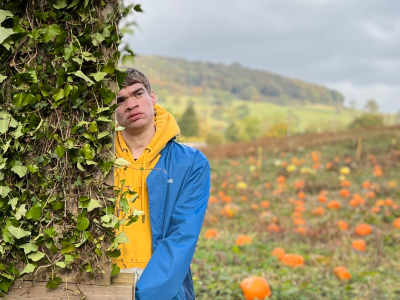 A boy by an arch of ivy with pumpkins behind him in a field