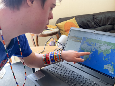 A boy wearing African jewellery looking at a map of Kenya on a laptop